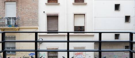 Ein Gebäude mit mehreren Fenstern, von denen einige mit Rollläden versehen sind, und einem Balkon mit Metallgeländer.