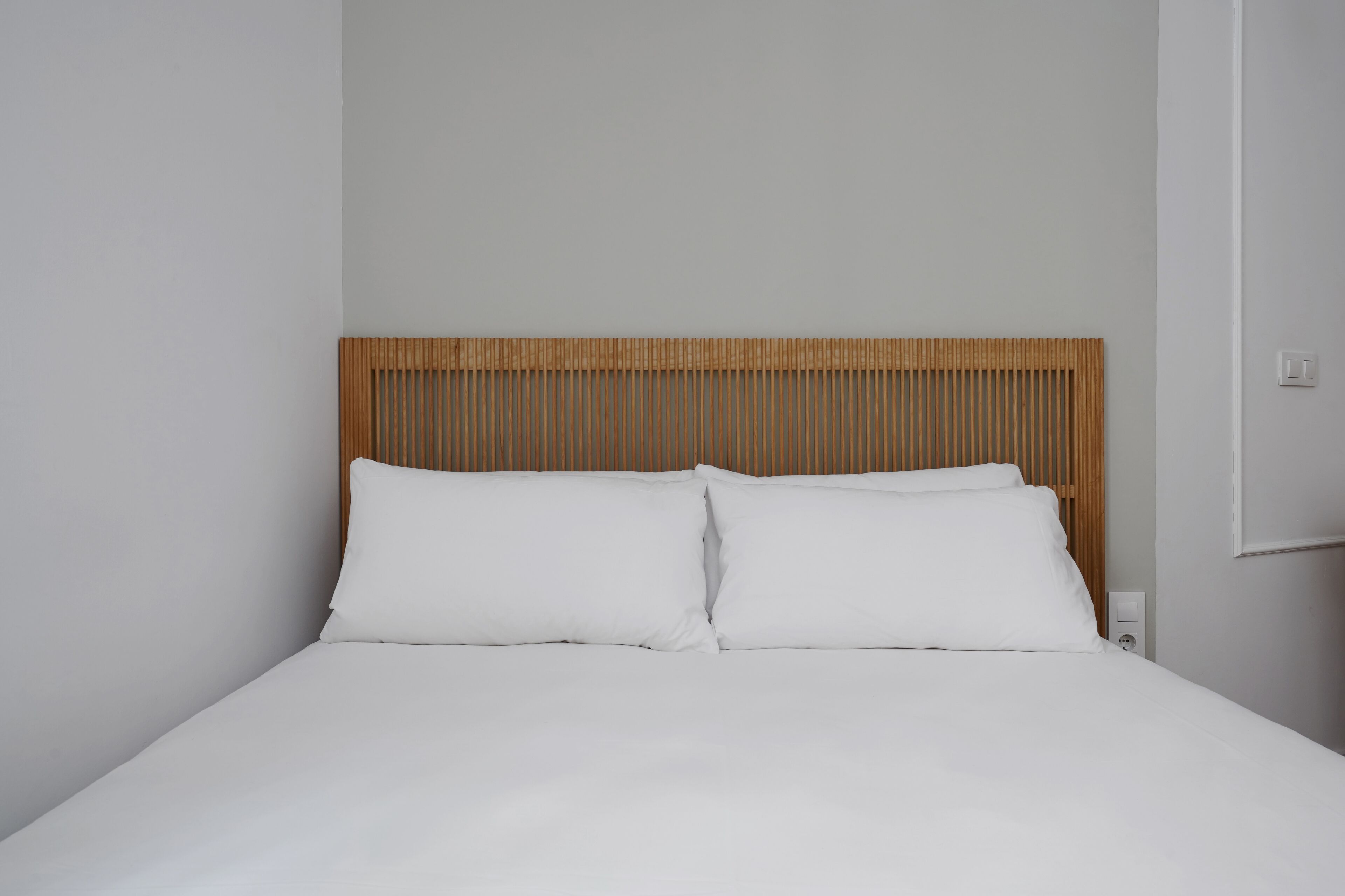 Una cama con sábanas blancas y cabecera de madera.