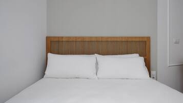 Una cama con sábanas blancas y cabecera de madera.