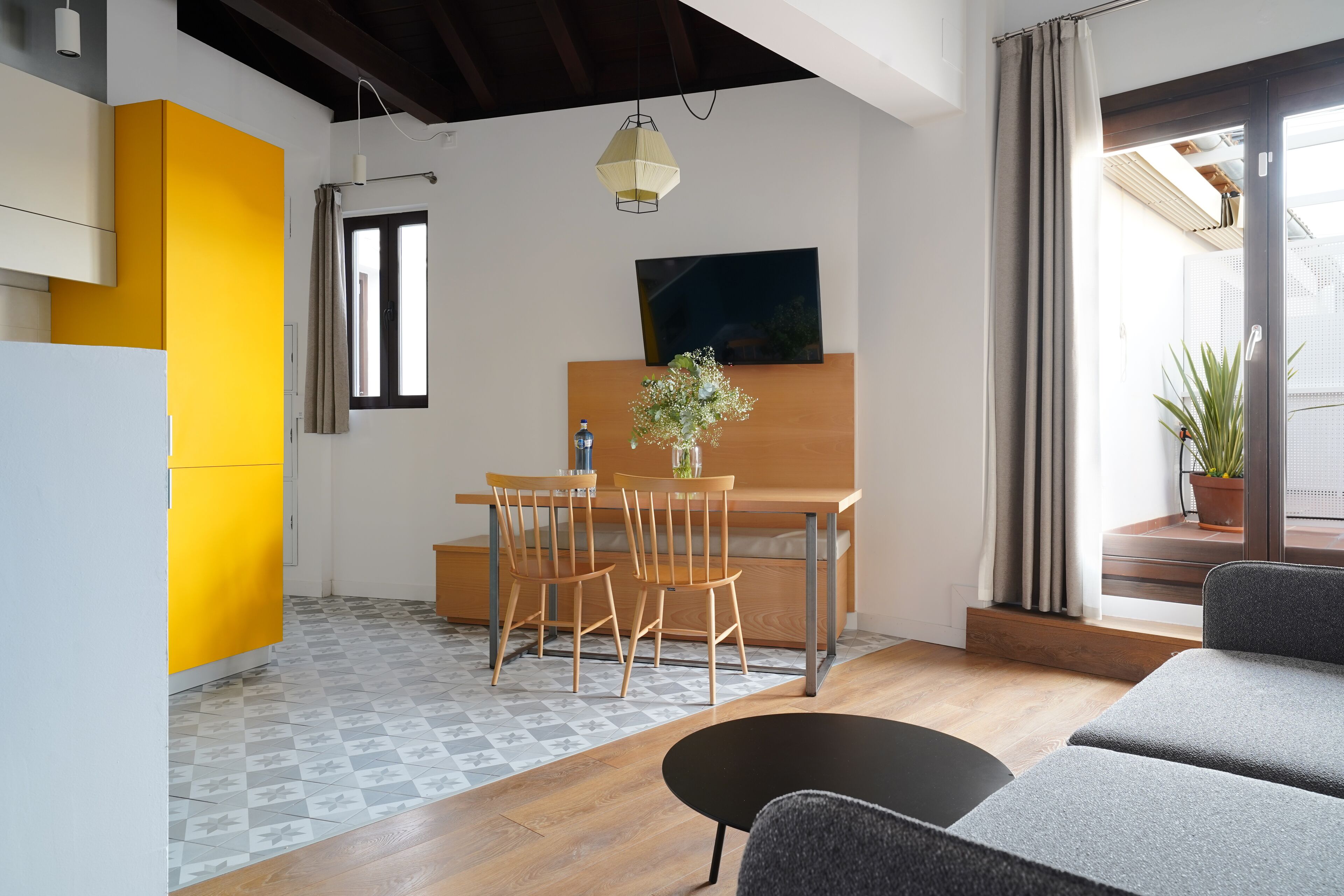 Una cocina moderna con una pared de acento amarilla, una zona de comedor con sillas de madera, una mesa negra y un sofá gris.