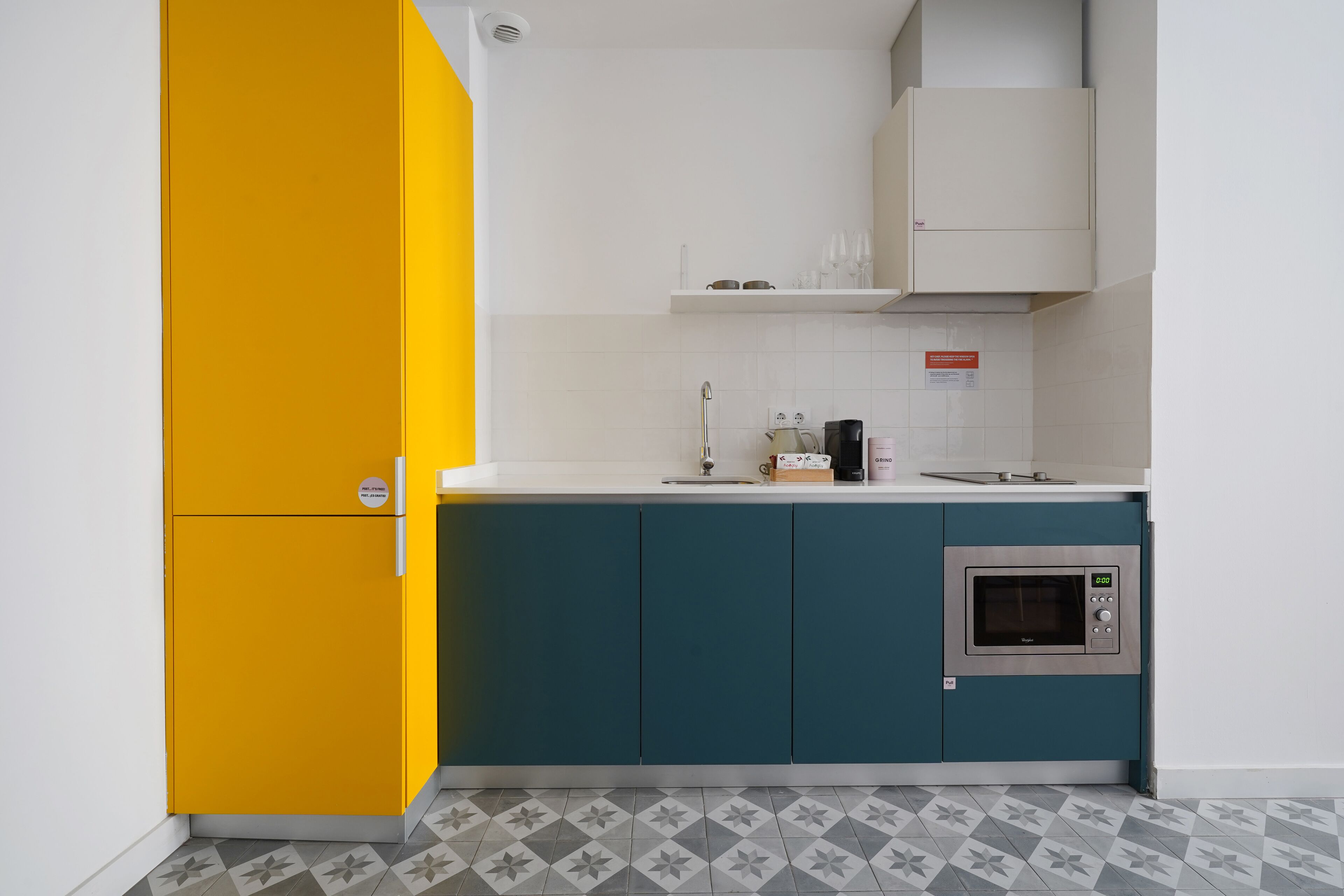 A kitchen with a yellow refrigerator, teal cabinets, a microwave, and a white countertop.