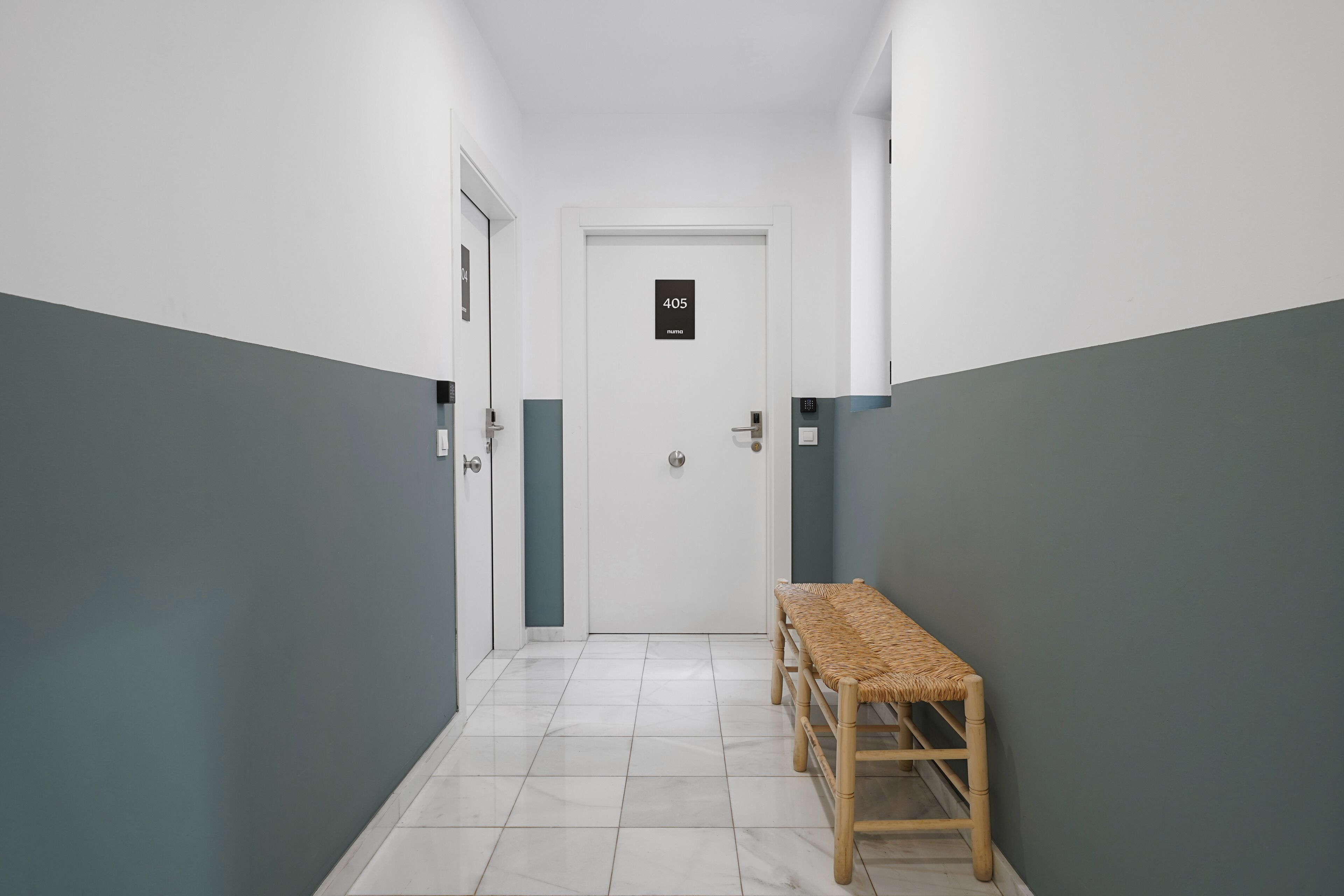 Un couloir avec une porte portant le numéro 405, un banc et un sol carrelé.