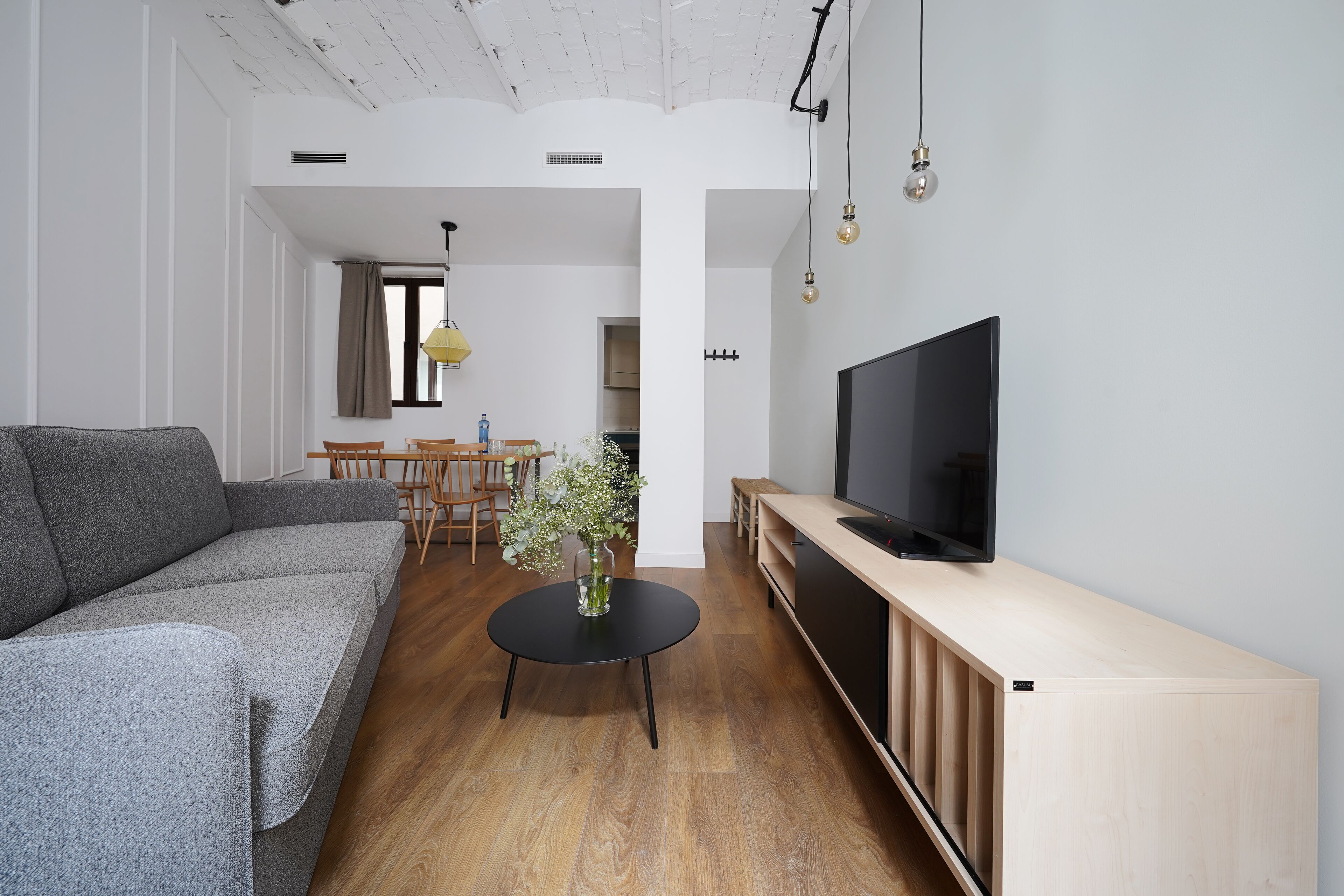 Una sala de estar moderna con un sofá gris, una mesa de centro negra y un televisor sobre un mueble de madera.