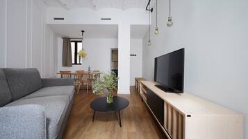 Una sala de estar moderna con un sofá gris, una mesa de centro negra y un televisor sobre un mueble de madera.