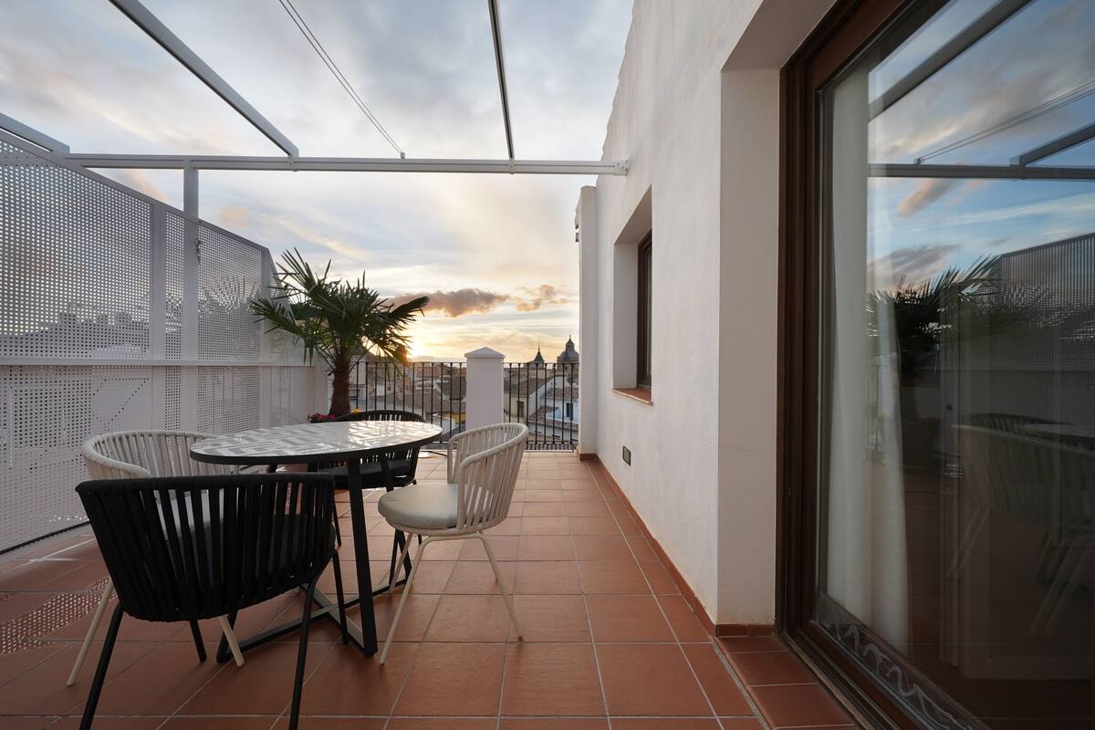 A balcony with a table and chairs, a potted plant, and a view of the cityscape.
