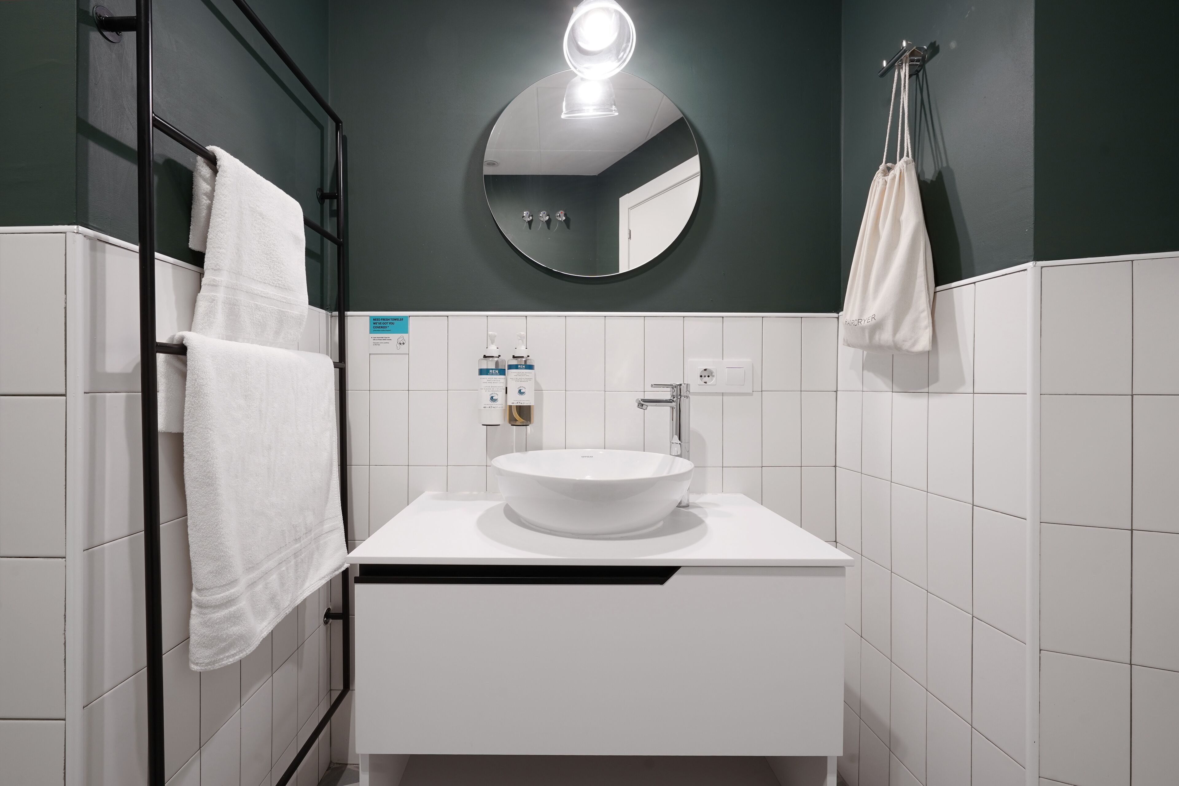 Un baño moderno con espejo redondo, lavamanos blanco y toallero.