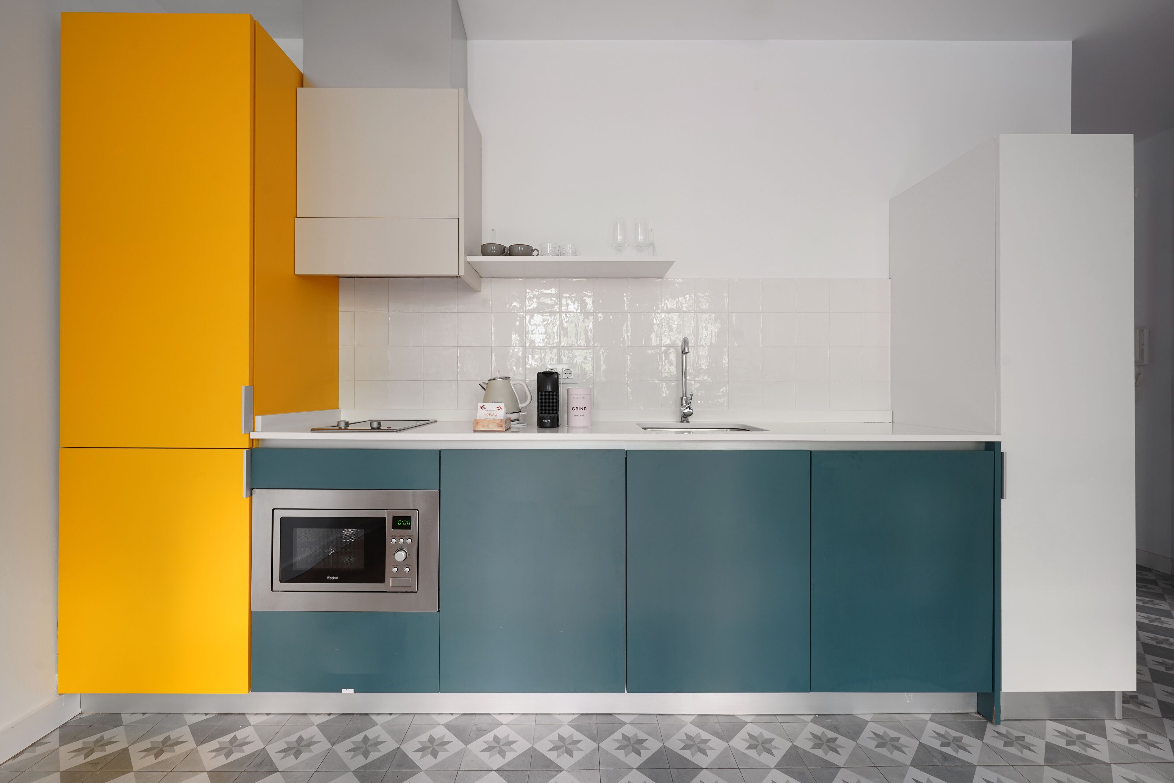 A modern kitchen with teal and yellow cabinets, a built-in oven, and a white countertop.