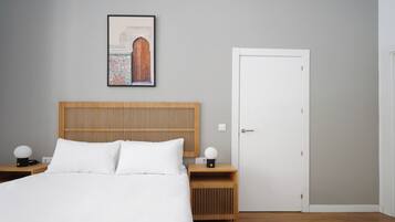 A modern bedroom with a wooden headboard, a white bed, two bedside tables with lamps, and a door.