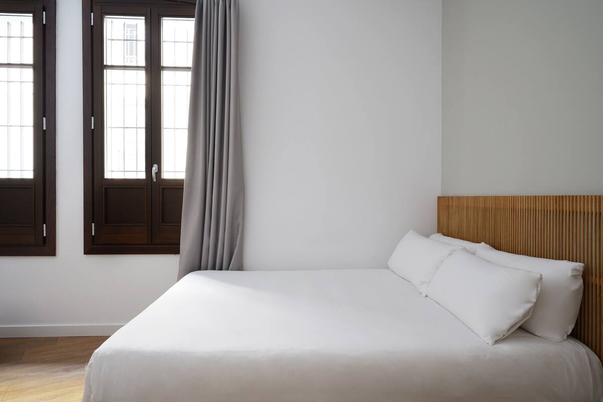 A bedroom with a bed, wooden headboard, and a window with curtains.