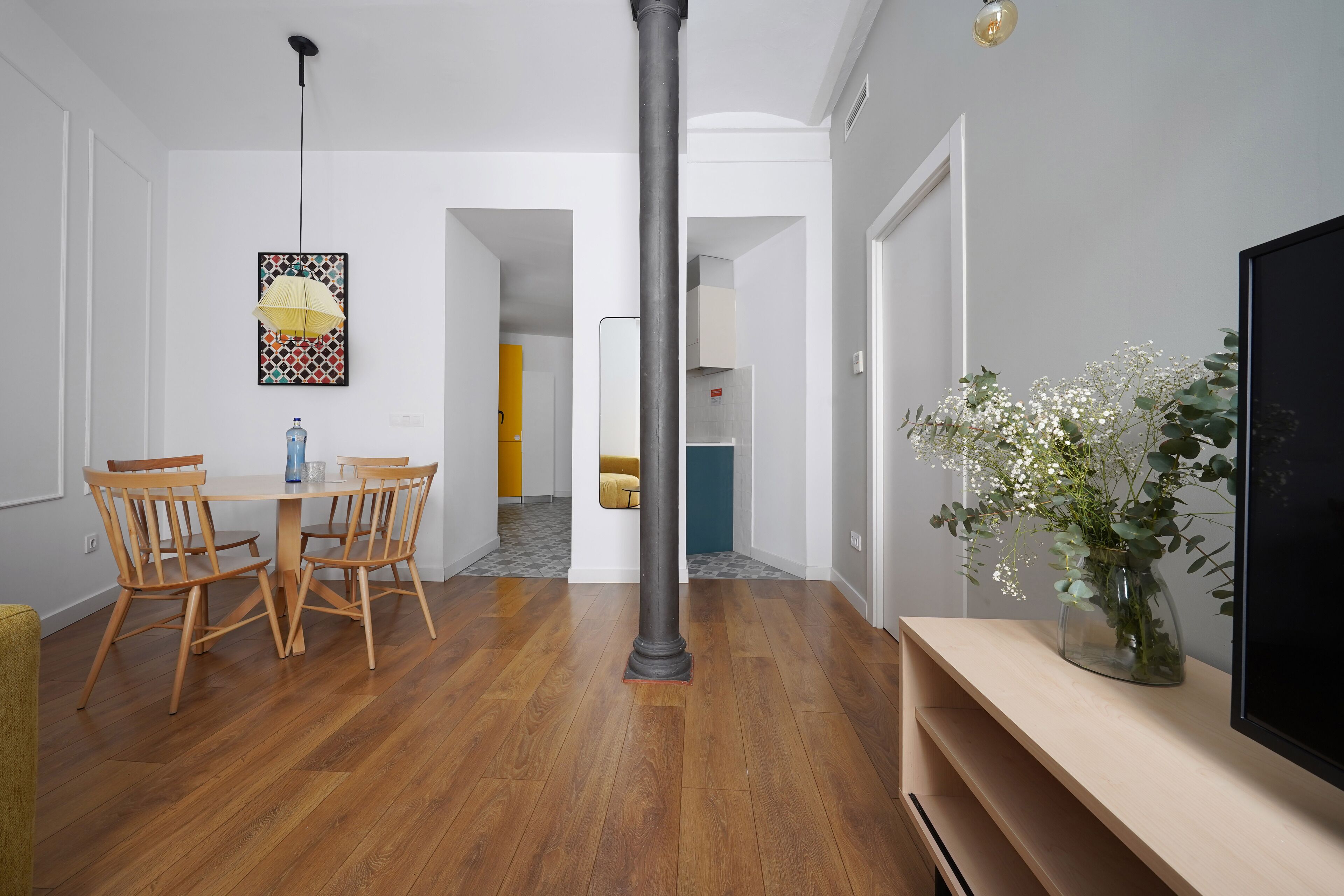 A dining area with a wooden table and chairs, a hanging light fixture, and a vase with flowers on a console table.