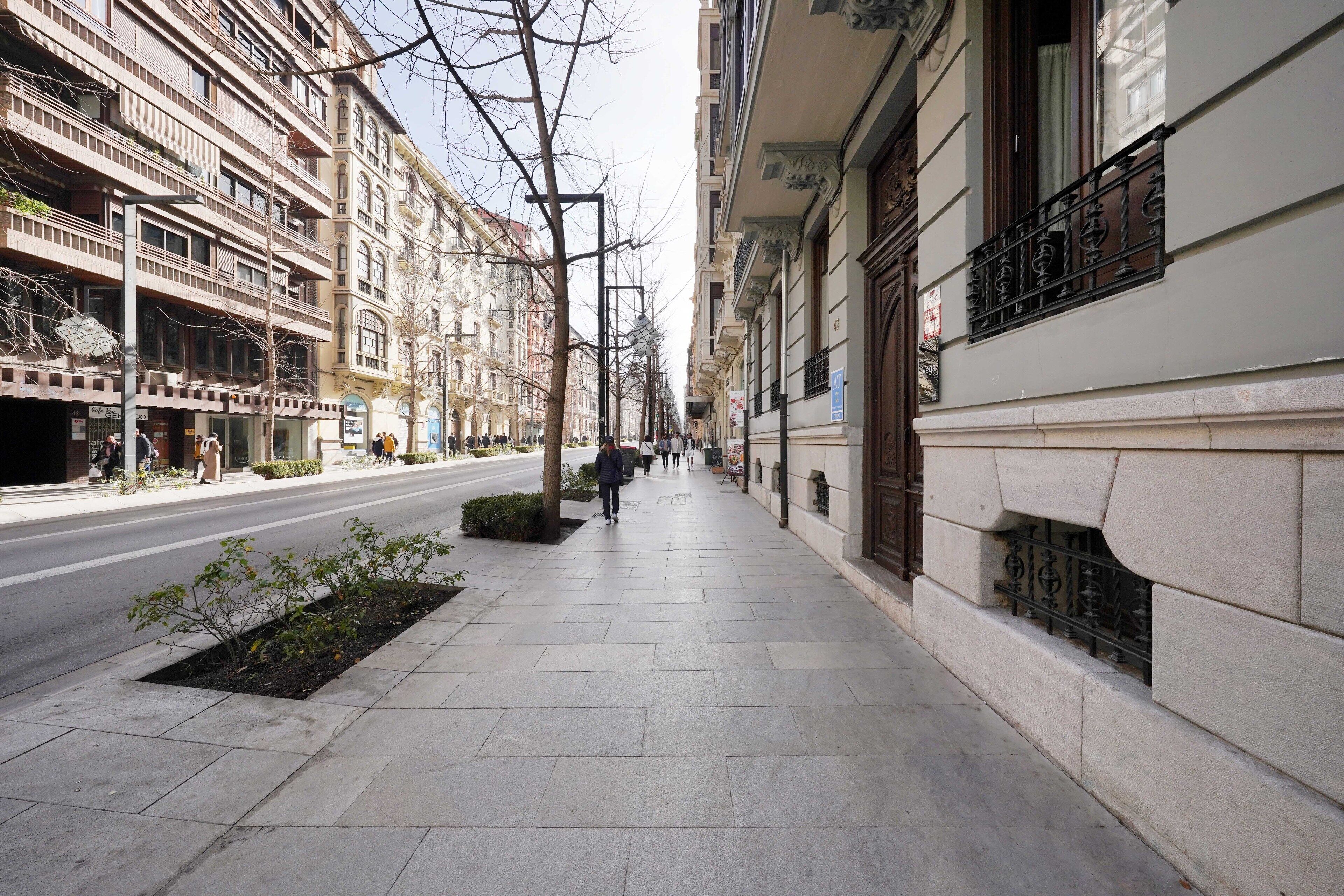 A city street with buildings on both sides, a sidewalk, and a few pedestrians.