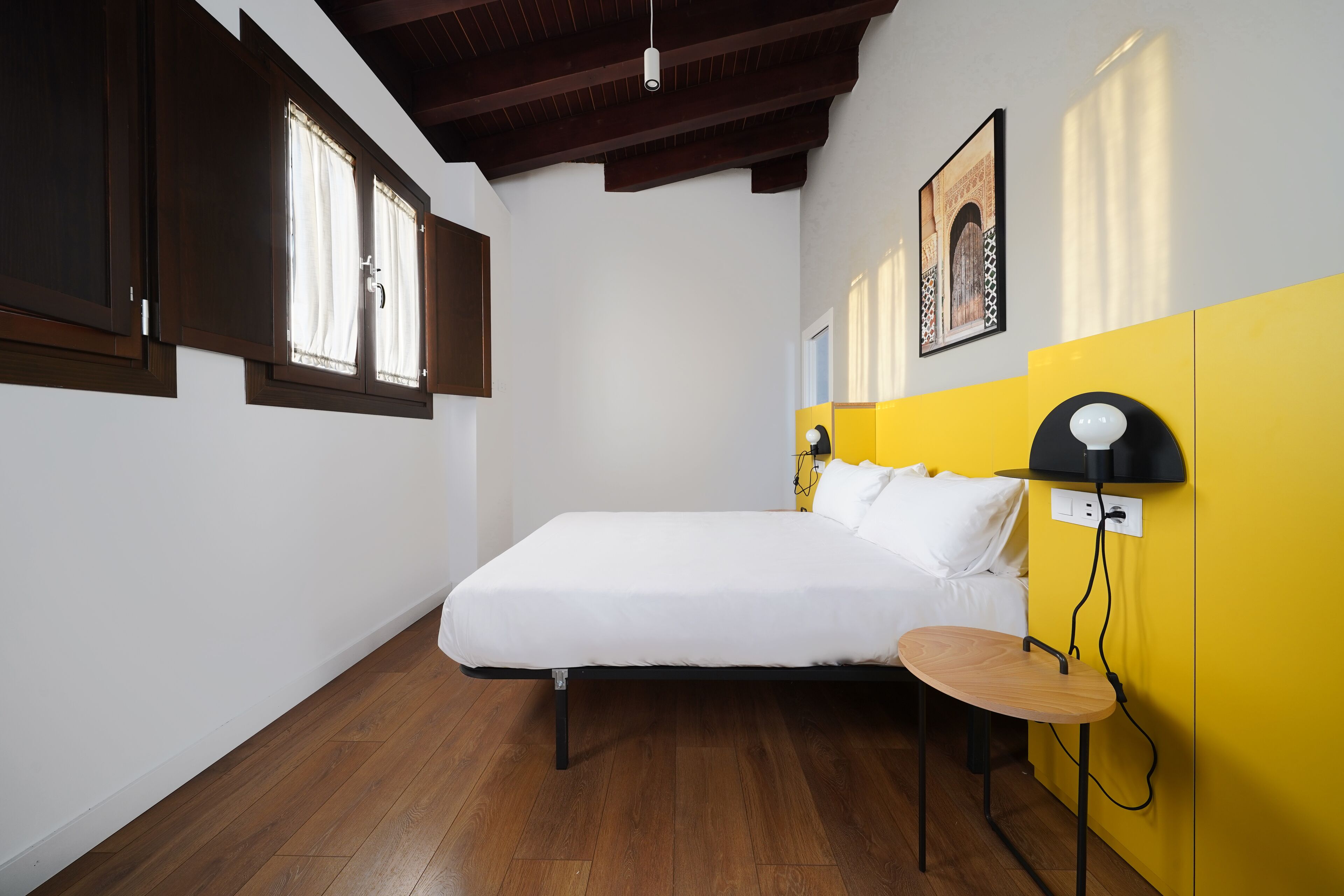 Un dormitorio con cama, mesita de noche, lámpara y ventana con cortinas.