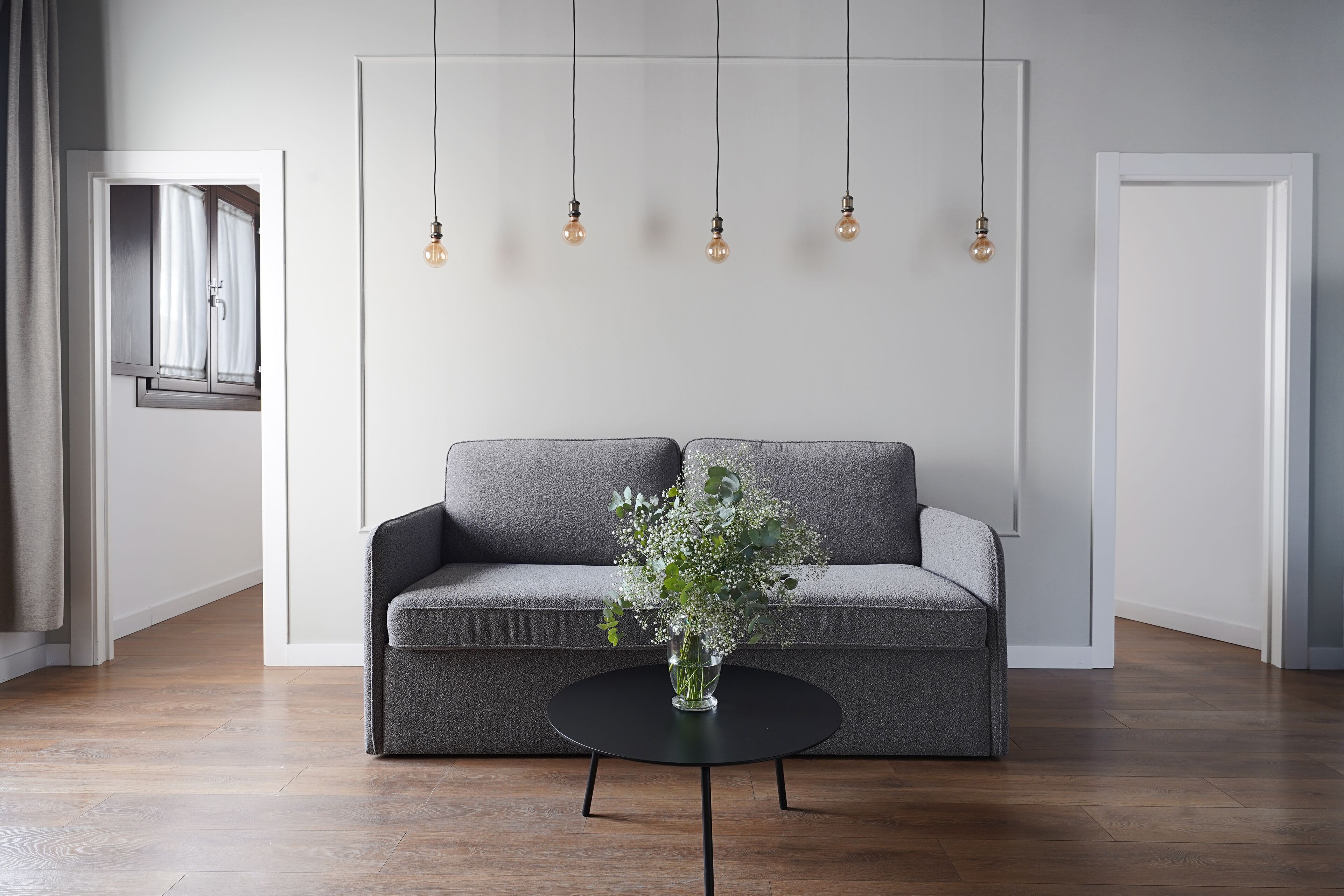 A modern living room with a grey sofa, a black coffee table, and a vase with flowers.