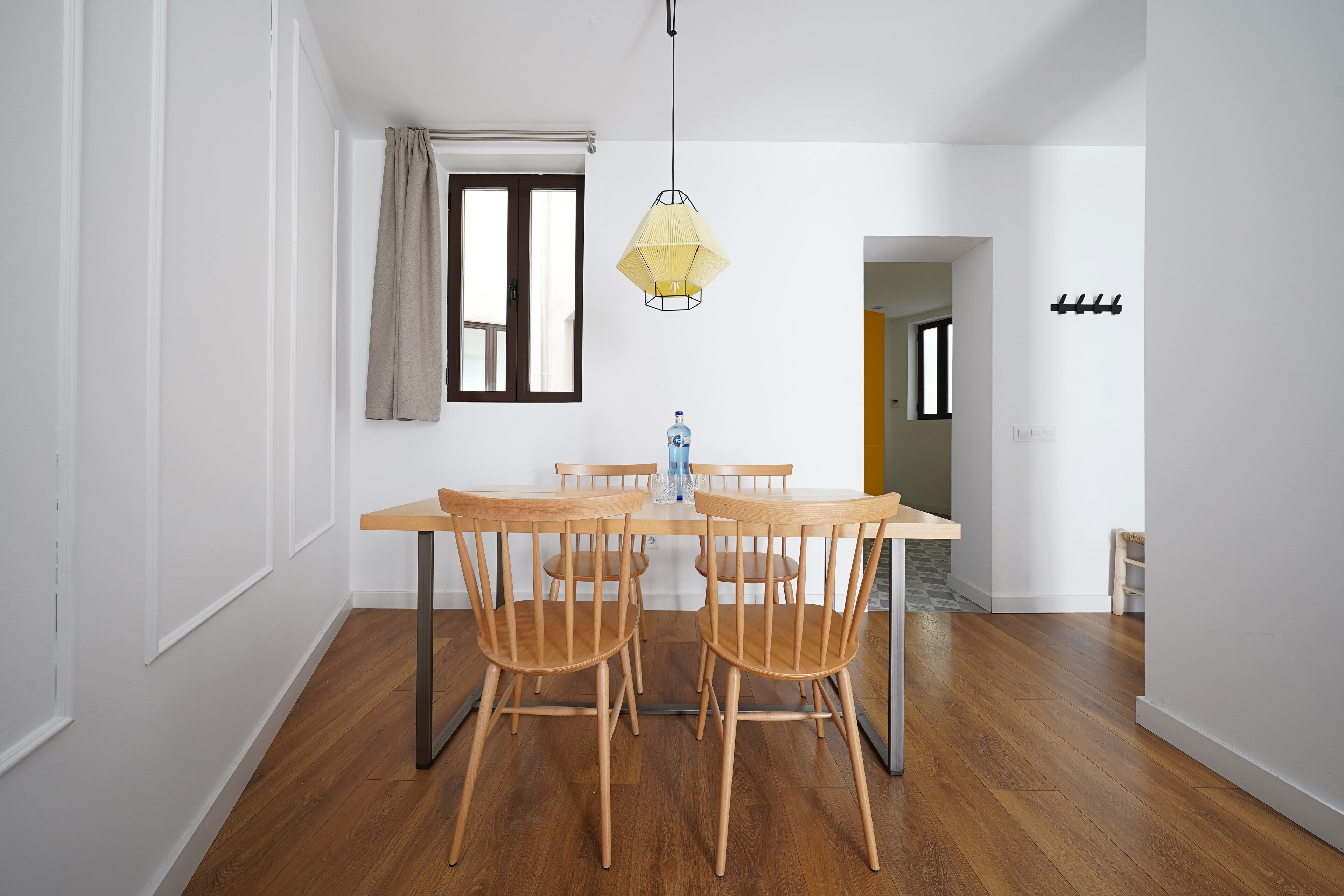Un coin repas avec une table et des chaises en bois, un luminaire suspendu et une fenêtre avec des rideaux.