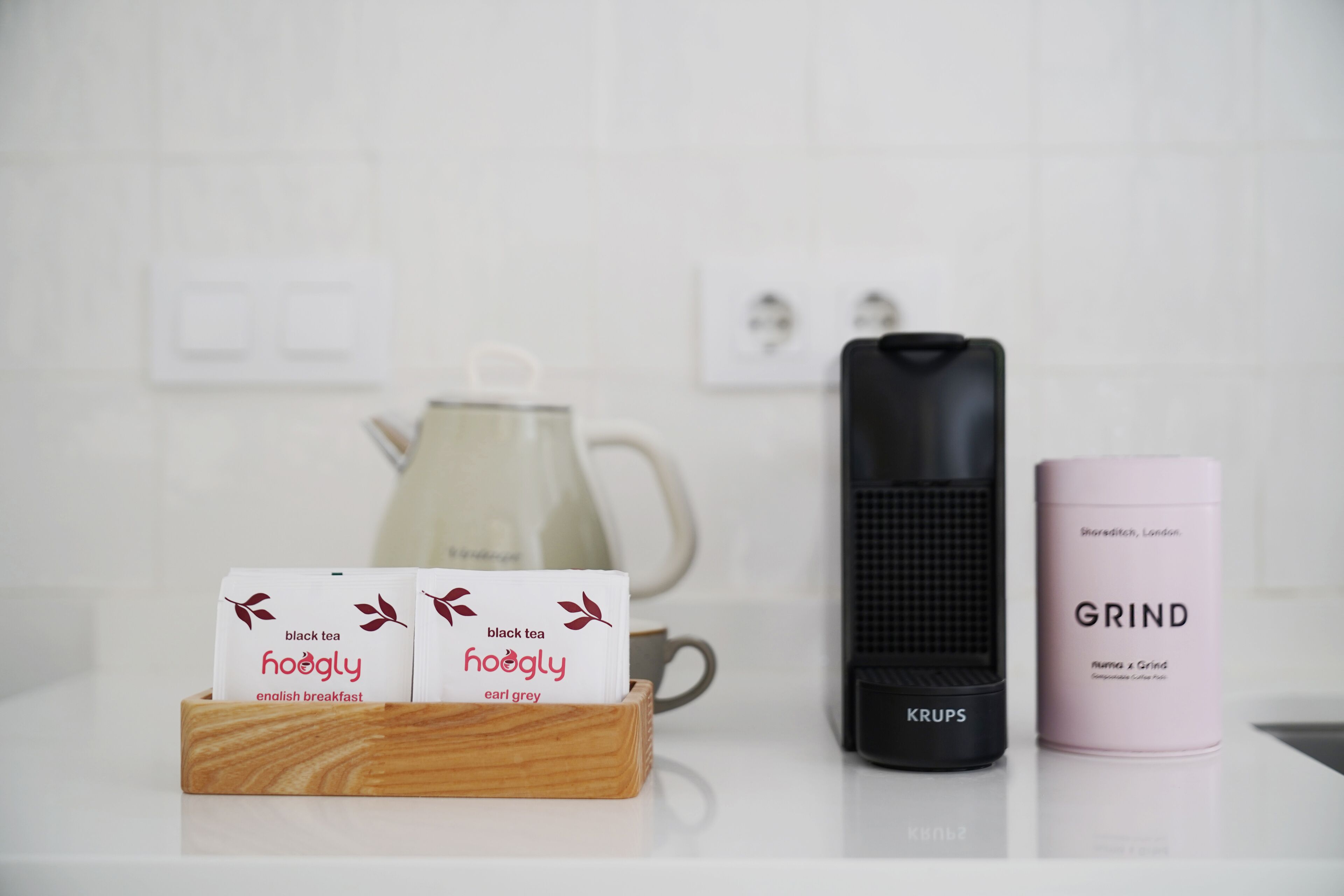 Una encimera de cocina con una cafetera, un hervidor y un recipiente etiquetado 'GRIND'.