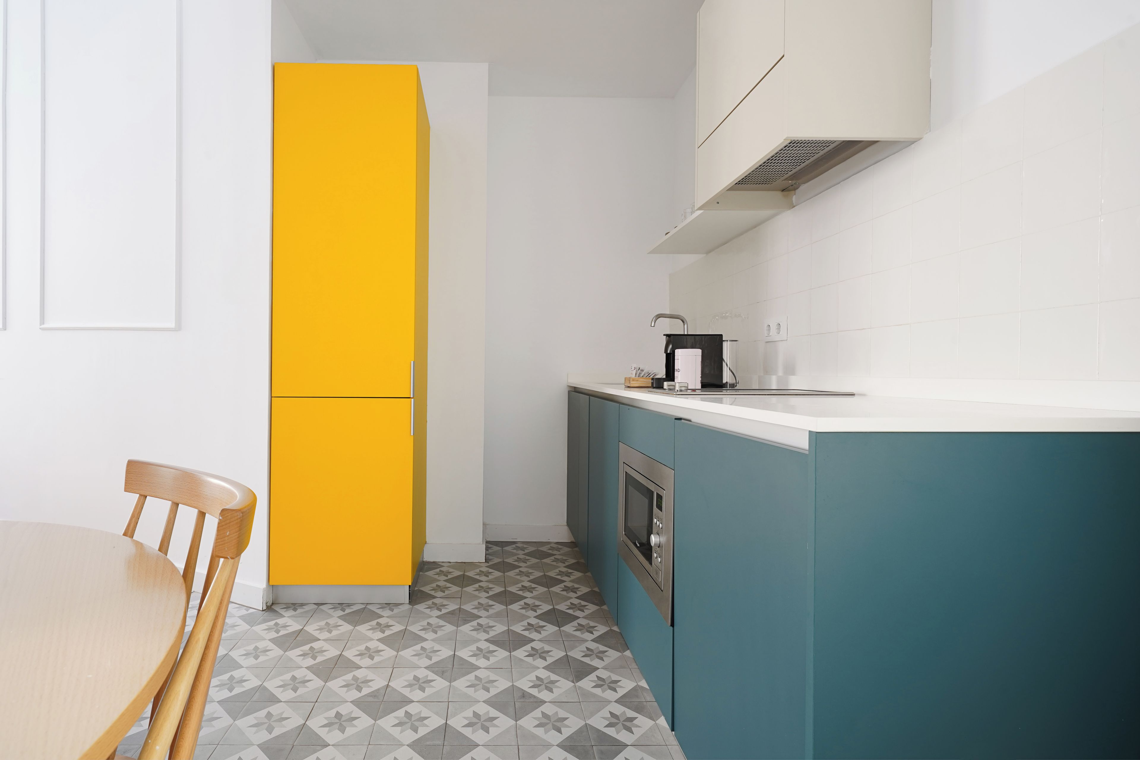 Una cocina compacta con un refrigerador amarillo, gabinetes verde agua y una encimera blanca.