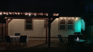Une terrasse extérieure dotée d’une pergola, d’une table, de chaises et de guirlandes lumineuses.