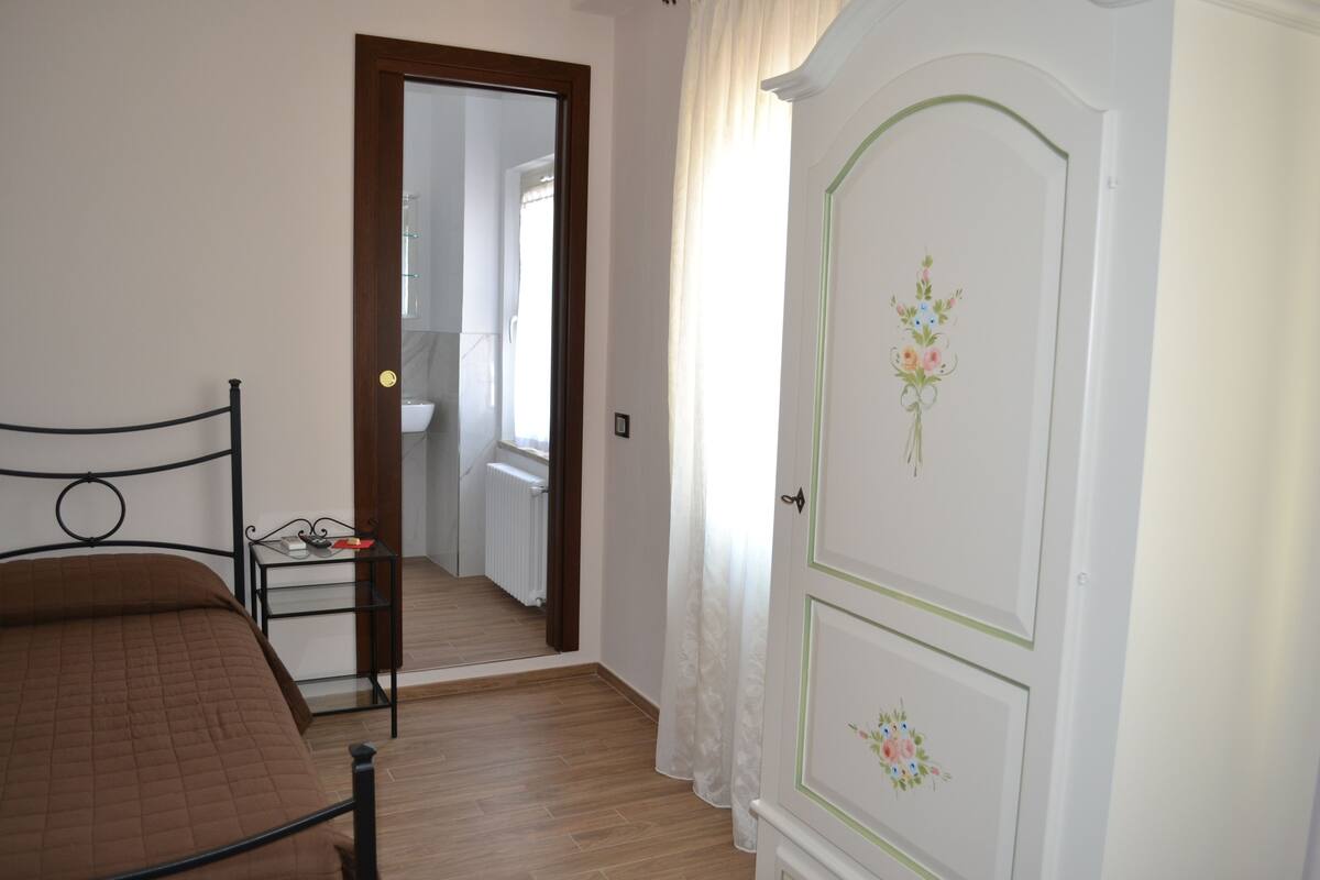 A bedroom with a bed, a wardrobe, and a bathroom visible through an open door.