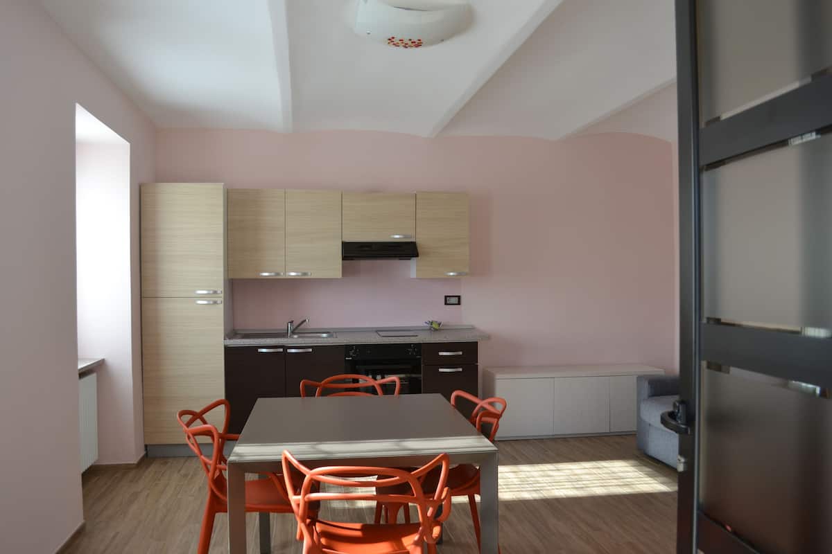 A modern kitchen with wooden cabinets, a dining table with orange chairs, and a refrigerator.