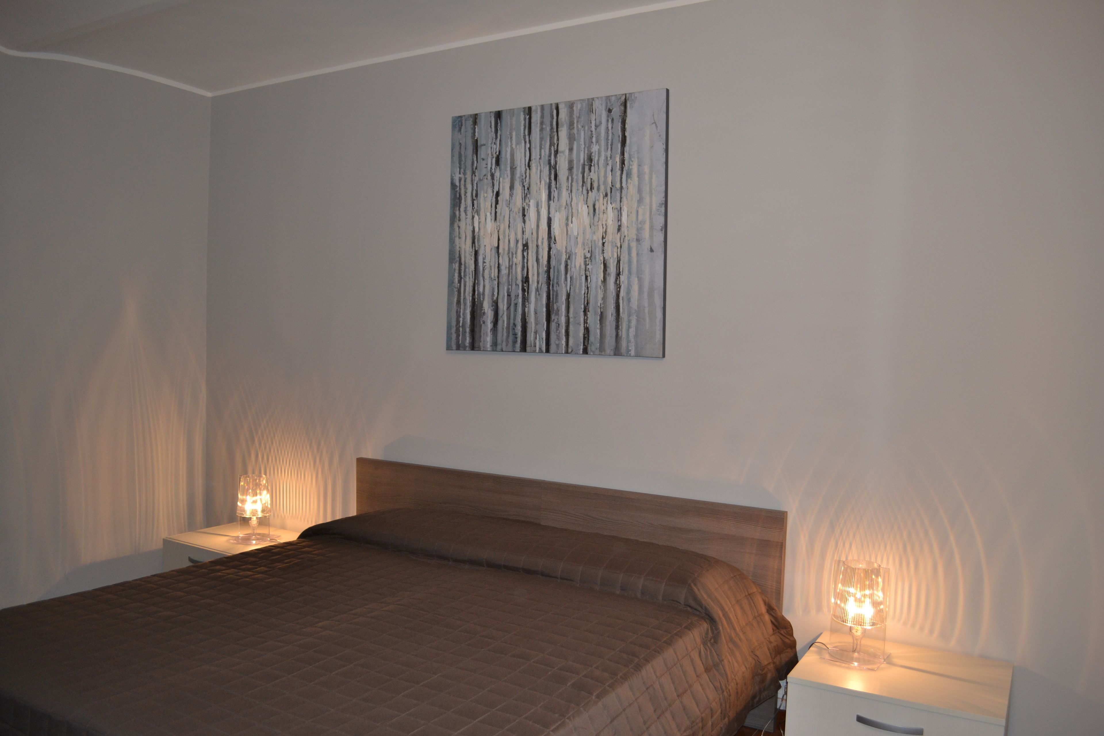 A bedroom with a bed, two bedside tables, and a wall-mounted artwork.