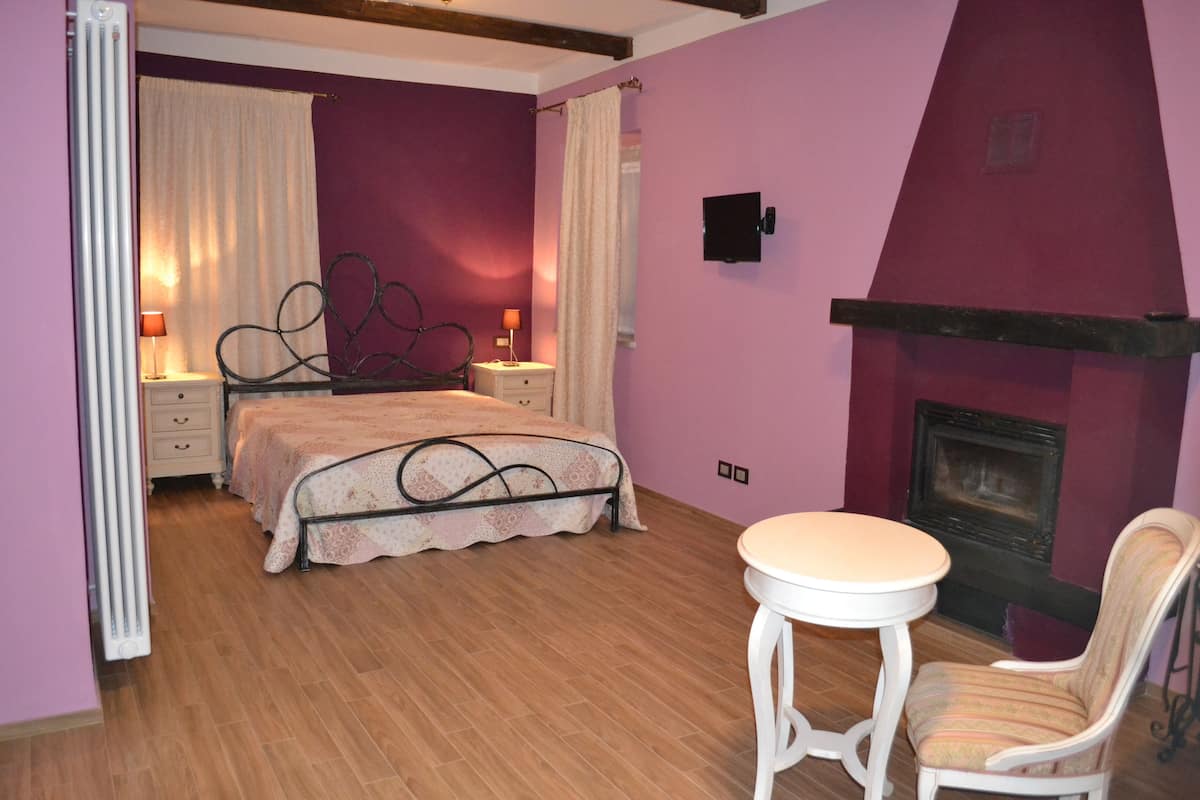 A bedroom with a bed, bedside tables, a chair, a fireplace, and a radiator.
