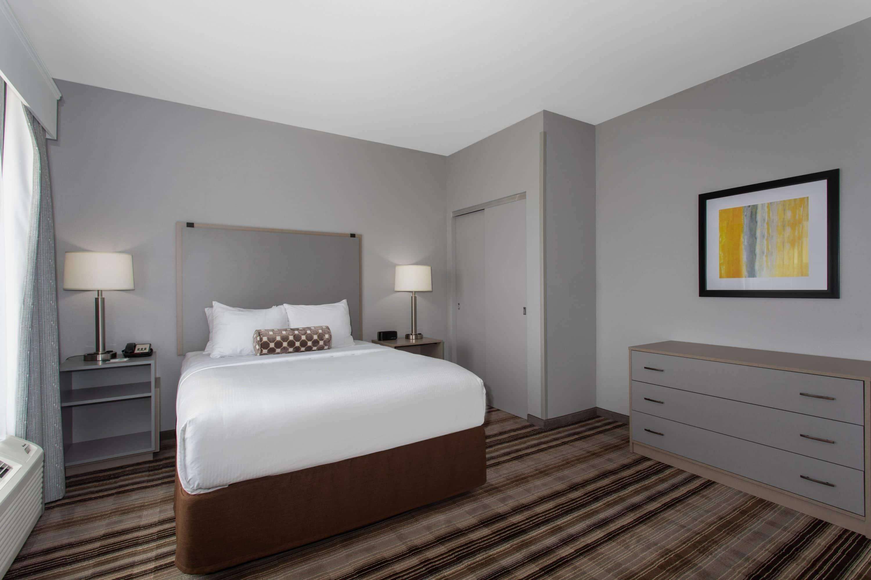A hotel room with a large bed, two bedside tables with lamps, a dresser, and a framed picture on the wall.