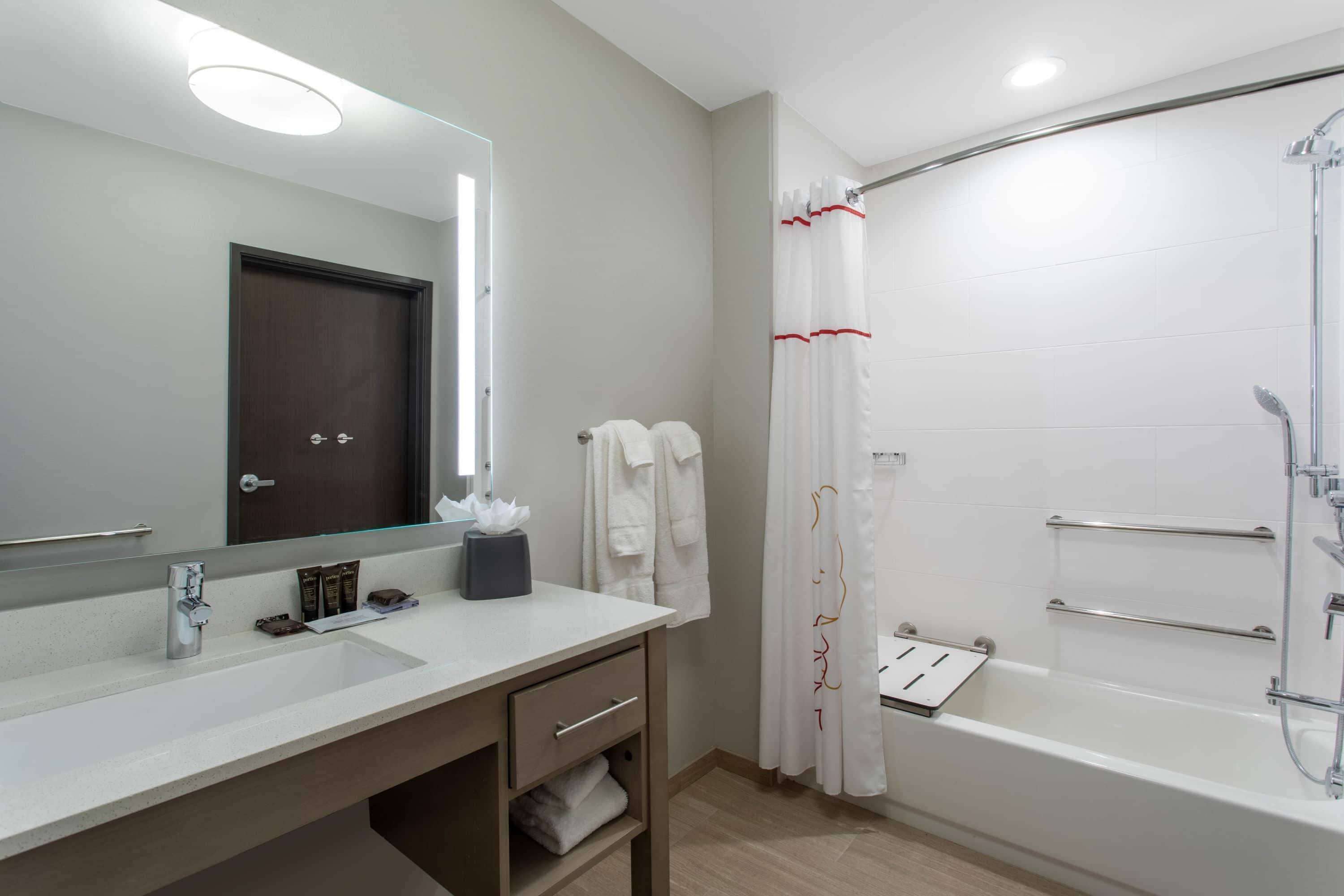 A modern bathroom with a large mirror, a sink, a vanity, a bathtub, and a shower.