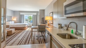 A hotel room with a bed, a desk, a chair, a TV, a sink, and a window with curtains. - Hawthorn Extended Stay by Wyndham Loveland (Loveland)