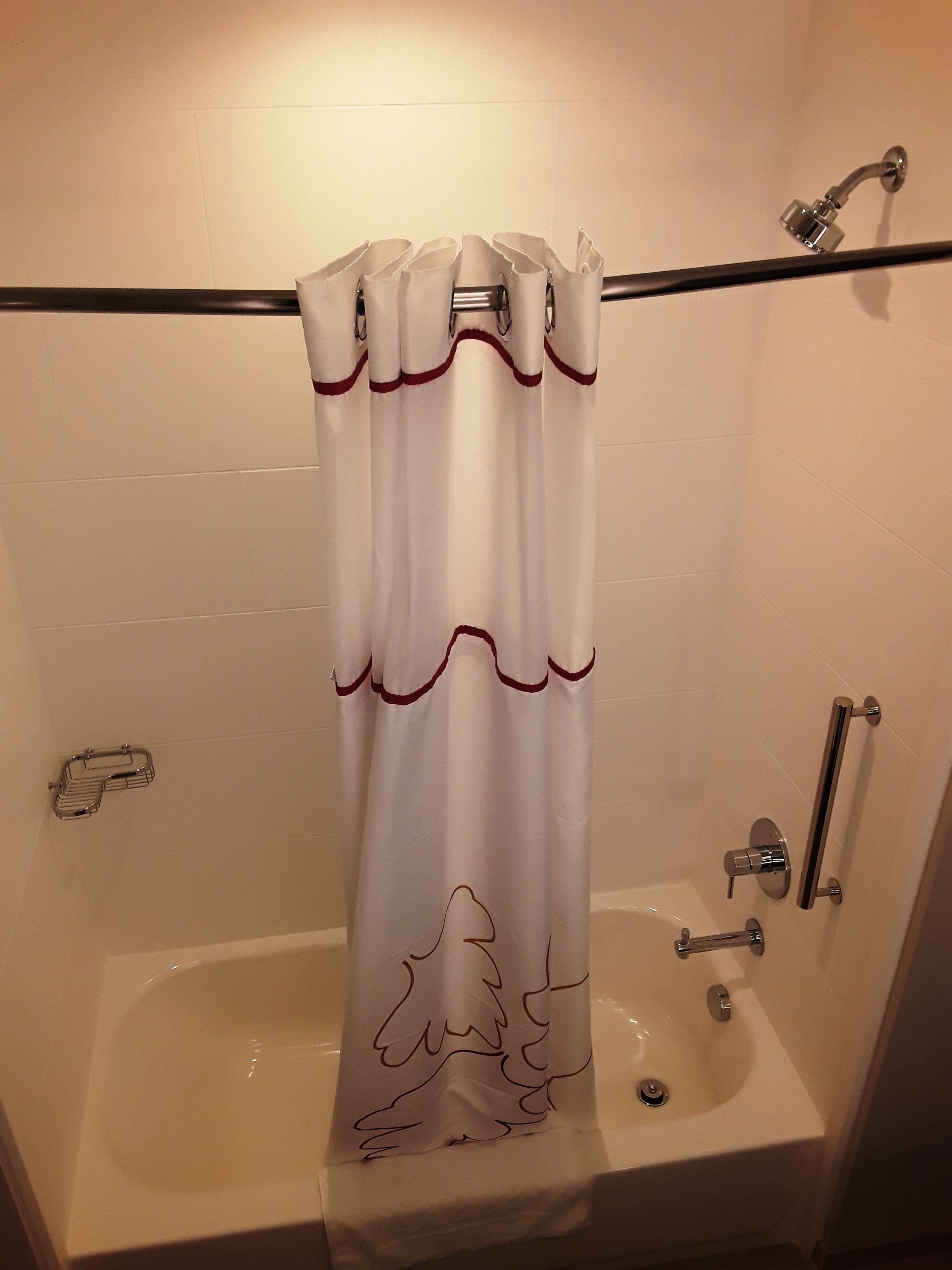 A bathroom with a bathtub, a shower curtain with a tree design, and a handrail.