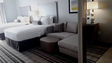 Una habitación de hotel con dos camas, un sofá, un pequeño reposapiés, una mesita de noche con lámpara y un cuadro en la pared.