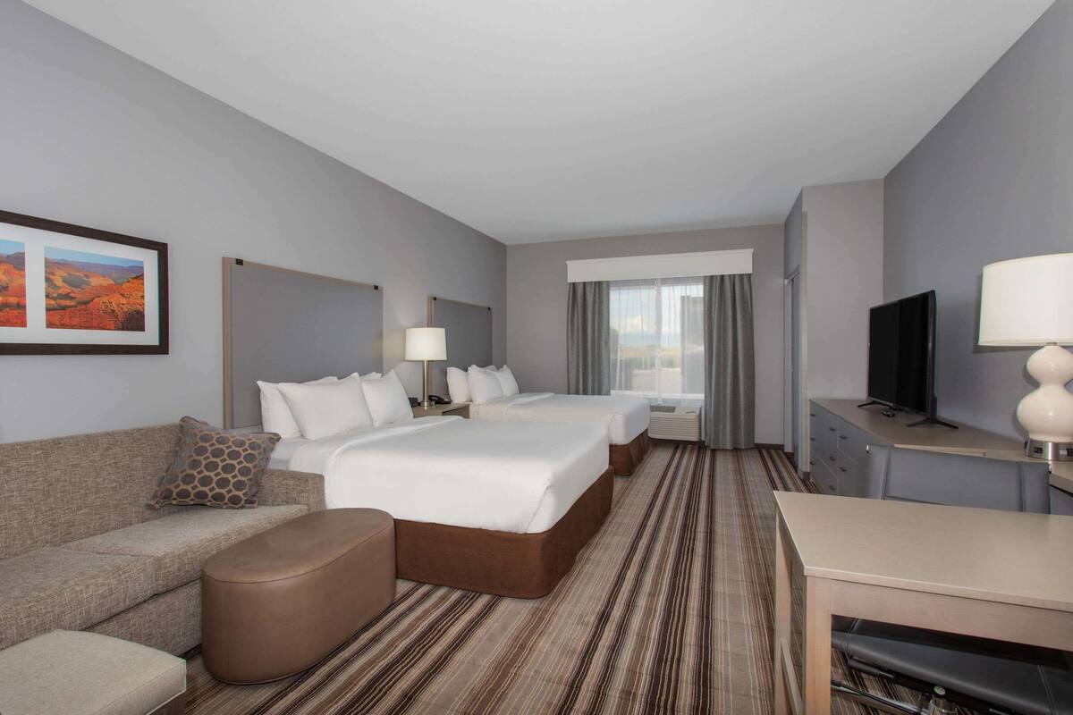 Een hotelkamer met twee bedden, een sofa, een bureau en een televisie.