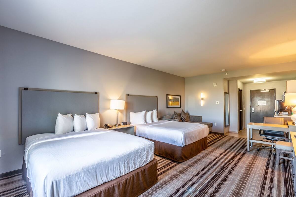 Een hotelkamer met twee bedden, een bureau, een stoel, een lamp en een schilderij aan de muur.