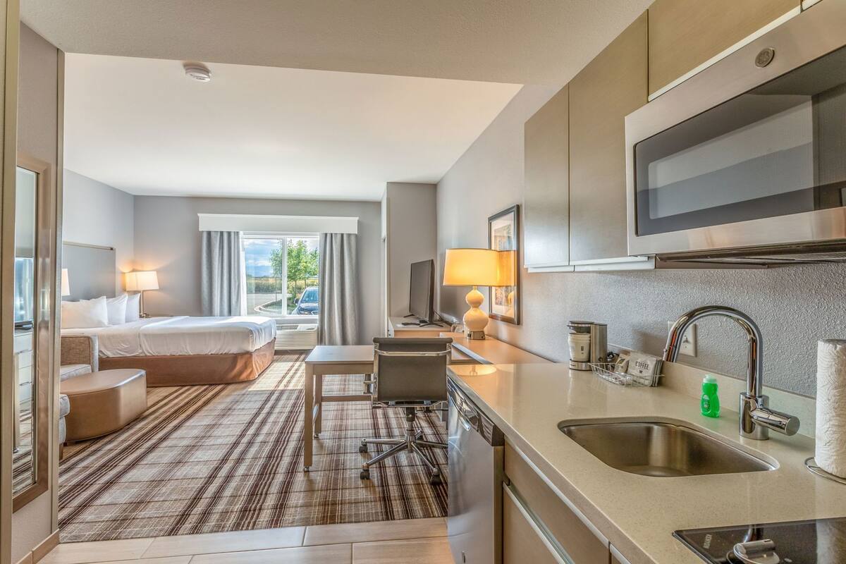 Hotelkamer met een bed, bureau, stoel, kleine kitchenette en raam met gordijnen.