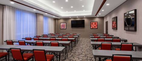 A conference room with tables and chairs, a flat-screen TV, and artwork on the walls.