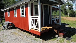 A red and white wooden cabin with a porch, a small table, and chairs. - Holiday Home Sundslätt (Urshult)