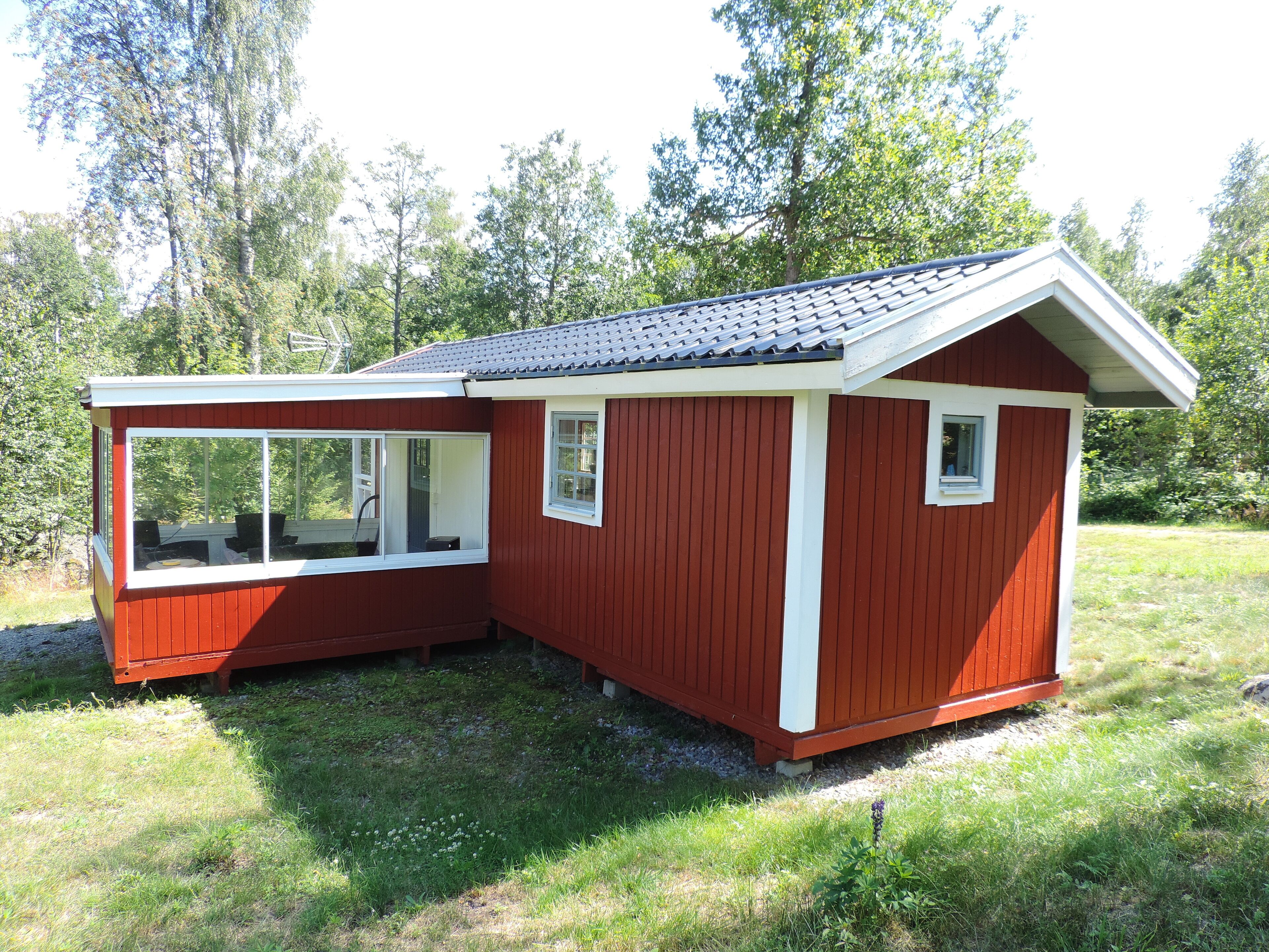 A small, red wooden cabin with a sloped roof, a large window, and a small door.