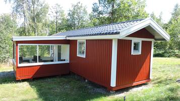 A small, red wooden cabin with a sloped roof, a large window, and a small door.