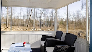 A covered outdoor seating area with a table and chairs, large windows offering a view of a wooded landscape. - Holiday Home Sundslätt (Urshult)