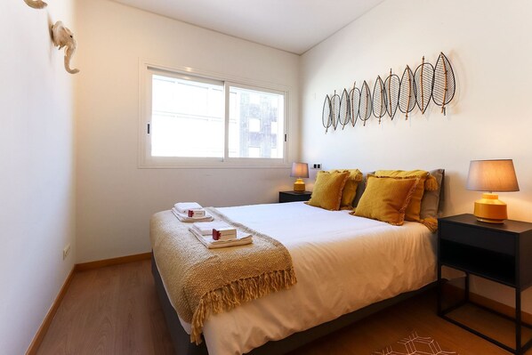 Un dormitorio ordenado con una cama grande, dos mesitas de noche, una ventana con persianas y un adorno en la pared.