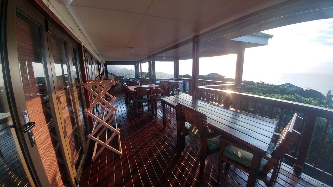 Una terraza de madera con mesas y sillas, con vistas panorámicas a colinas y al mar.