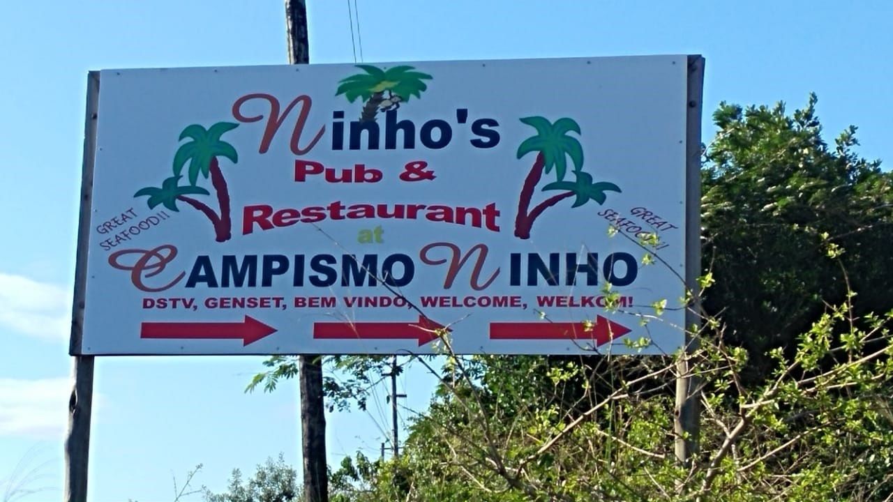 A sign for Ninho's Pub & Restaurant at CAMPISMO INHÓ, with directional arrows and welcoming text.