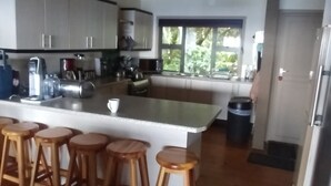A kitchen with a central island, wooden stools, and a window with a view of greenery. - Campismo Ninho 23 (Ponta d'Ouro)