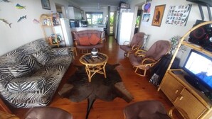 A living room with a zebra-patterned sofa, a brown leather couch, and wicker chairs. A wooden coffee table is in the center. - Campismo Ninho 23 (Ponta d'Ouro)