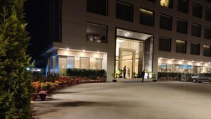 A modern hotel entrance at night with a well-lit facade, a covered outdoor area with potted plants, and a parking area. - Novanta Jamshedpur (Adityapur)