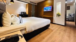 A modern hotel room with a large bed, a TV mounted on the wall, a desk with a phone, and a small table with flowers. - Novanta Jamshedpur (Adityapur)