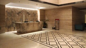 A lobby with a reception desk, a patterned floor, and a large window. - Novanta Jamshedpur (Adityapur)