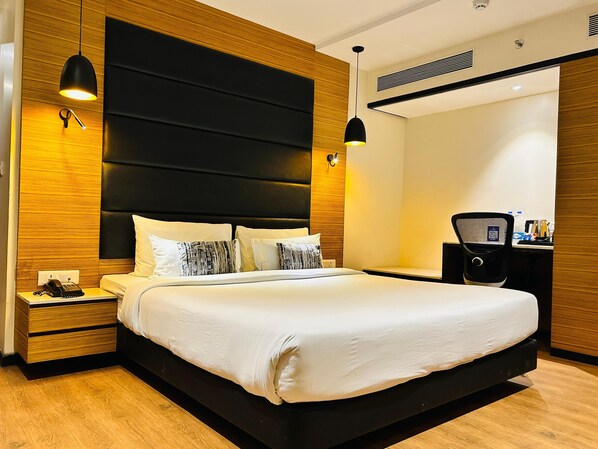 Quarto de hotel moderno com uma cama grande, cabeceira de madeira, mesas de cabeceira e uma escrivaninha com cadeira.