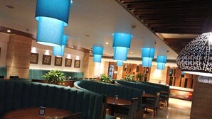 A restaurant with round tables and booths, blue hanging lamps, and framed artwork on the walls. - Novanta Jamshedpur (Adityapur)
