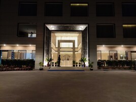 Una entrada de edificio moderna con fachada de vidrio, plantas en macetas y una persona de pie en el umbral.