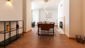 Un espace repas moderne avec une table en bois dressée pour quatre personnes, entourée de chaises. Une étagère en métal noir, agrémentée d’objets décoratifs, se trouve à gauche.
